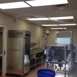 An industrial kitchen with stainless steel appliances and bright lighting.