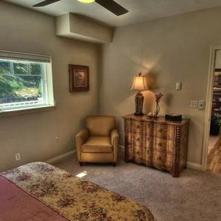 A cozy bedroom featuring a single chair, a dresser with a lamp, and a window letting in natural light.