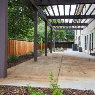 A modern backyard patio featuring a pergola and wooden fencing, surrounded by landscaped garden beds.