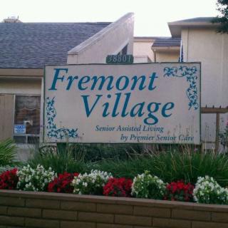A sign for Fremont Village in front of a building and flower garden.