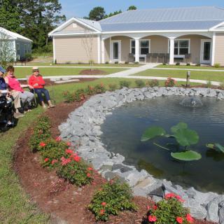 A group of people sitting by a landscaped garden with a pond in front of a house.