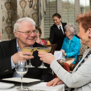 A senior couple is enjoying a celebratory toast at a restaurant, served by attentive waitstaff.