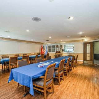 A spacious meeting room with blue tablecloths covering long conference tables surrounded by chairs, featuring a wooden floor and interior lighting.