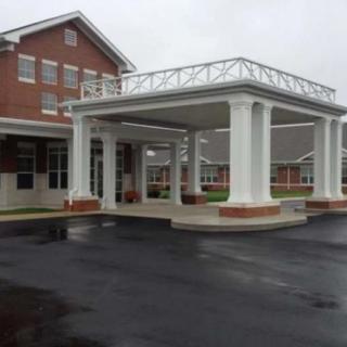 A building entrance with a covered canopy supported by white columns on an overcast day.