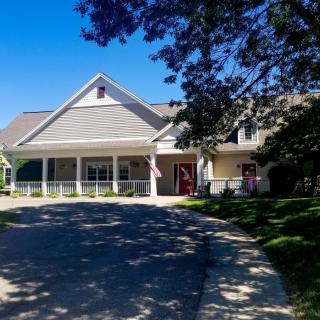 A charming house with a spacious driveway and surrounding trees under a clear blue sky.