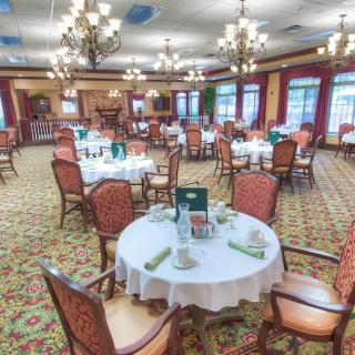 A beautifully arranged dining room with elegant chandeliers, round tables set for meals, and a plush carpeted floor.