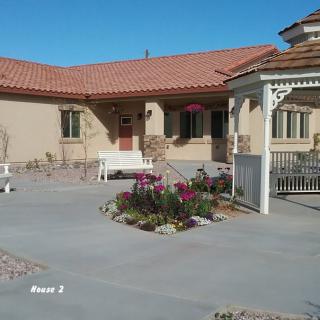 A quaint house with a patio and gazebo, surrounded by a small garden of flowers.