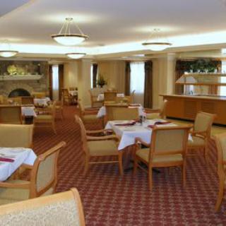 A spacious dining area with neatly arranged tables and chairs, featuring a warm, carpeted floor and elegant chandeliers.