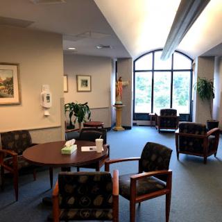 A cozy waiting room with comfortable seating, a round table, and natural light streaming through large windows.