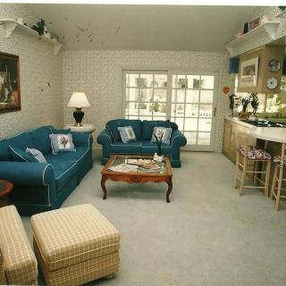 A cozy living room with a blue sofa set, coffee table, and a bar area by the windows.