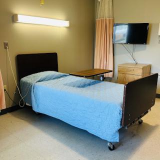 A hospital room featuring a bed with blue linens and a wall-mounted television.
