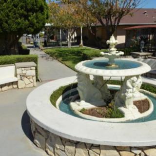 A beautifully landscaped garden featuring a central fountain surrounded by trees and a walkway.