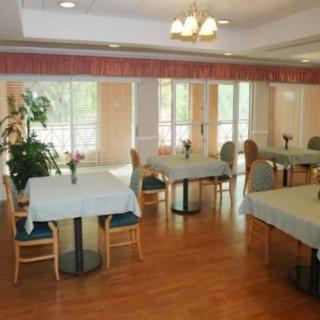 A spacious dining room with neatly arranged tables and chairs, adorned with plants and large windows providing natural light.