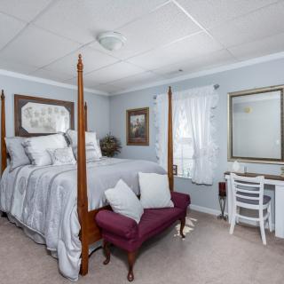A cozy bedroom with a four-poster bed, desk, and mirror, featuring light blue walls and elegant decor.
