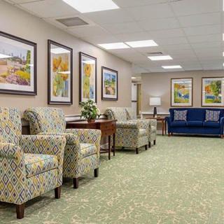 A well-lit waiting room with patterned chairs, a blue sofa, and landscape paintings on the walls.