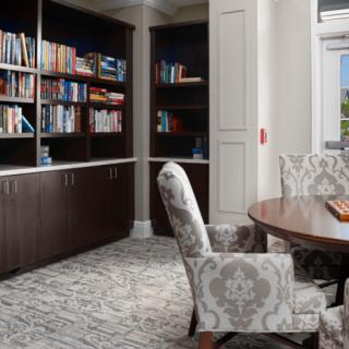 A cozy library corner with shelves full of books, a round table, and patterned chairs.