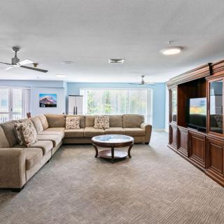 A spacious living room with a large sectional sofa, coffee table, and entertainment center, beautifully lit by natural light streaming through the windows.