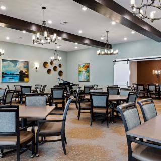 A spacious dining room with elegant chandeliers, neatly arranged tables and chairs, and decorative artwork on the walls.