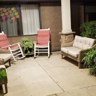 A cozy outdoor seating area with rocking chairs and a couch, surrounded by greenery at night.