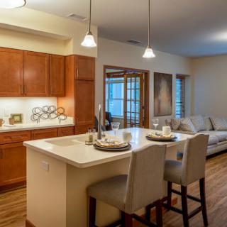 A stylish open-concept kitchen and living area featuring wooden cabinetry, modern bar stools, and inviting lighting.