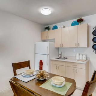 A cozy kitchen and dining area featuring a wooden table set with plates and cups, complemented by light-colored cabinets and a refrigerator.