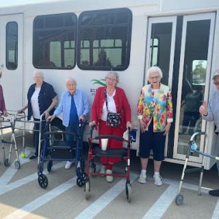 A joyful group of seniors ready for their day out, supported by mobility aids.