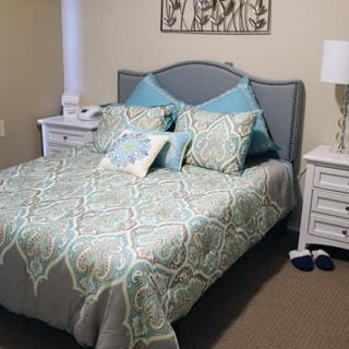 A neatly arranged bedroom with a bed featuring patterned bedding and pillows, flanked by two nightstands and a lamp.