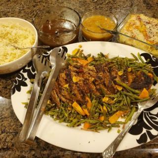 A dinner spread featuring a platter of grilled meat with vegetables, mashed potatoes, and sauces.