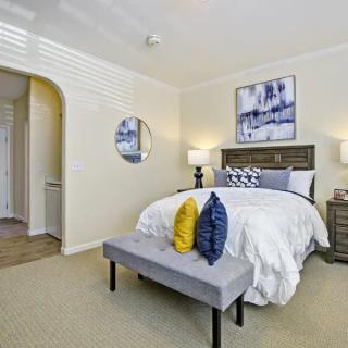 A cozy bedroom with tasteful decor, featuring a bed adorned with colorful pillows, side tables with lamps, and modern artwork on the walls.
