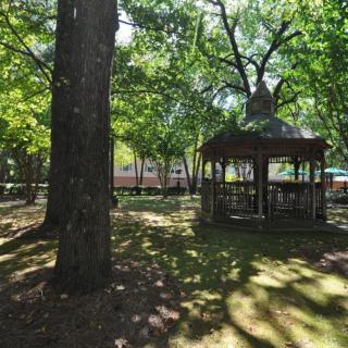 A serene park setting with a gazebo surrounded by trees and dappled sunlight.
