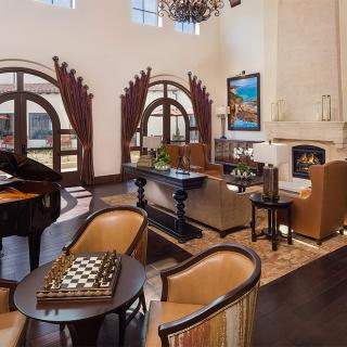 A luxurious living room featuring a grand piano, elegant seating area with a chess set, and a cozy fireplace beneath arched windows.