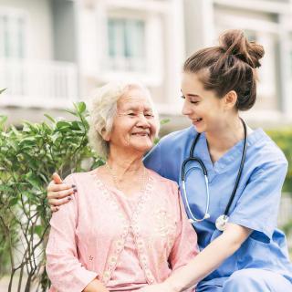 A nurse shares a joyful moment with an elderly woman outdoors.