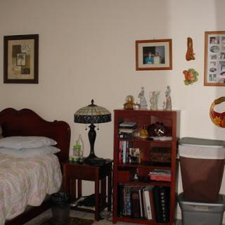 A cozy bedroom featuring a bed, bookshelf filled with books, and decorative items on the walls.