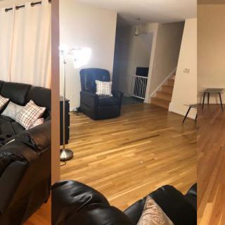 A cozy living room with a sofa, armchair, and floor lamp, featuring wood flooring and curtains.
