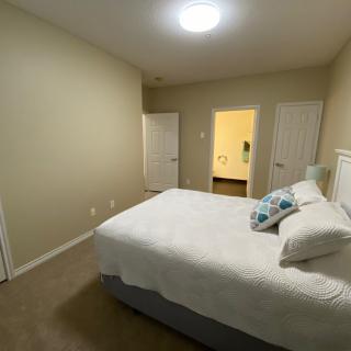 A minimalist bedroom with a neatly made bed, carpet flooring, and two doors leading to other rooms.