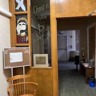 A view of an office space with wooden elements, artwork on the walls, and a doorway leading to another area.