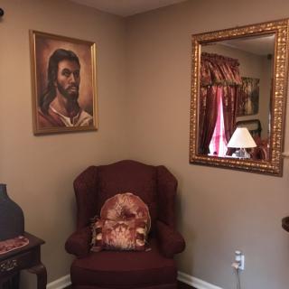 A cozy corner of a living room featuring an armchair, a painting on the wall, a decorative mirror, and a lamp.