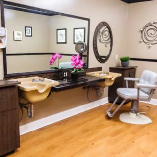 A modern salon interior featuring styling stations with mirrors, a barber chair, and decorative elements.