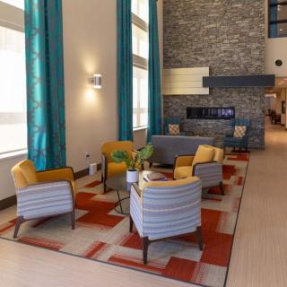 A modern living area with colorful chairs and a stone fireplace, featuring bright teal curtains and a vibrant rug.