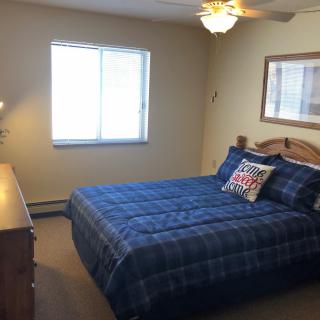 A cozy bedroom featuring a bed with blue plaid bedding, a wooden dresser, and a ceiling fan.