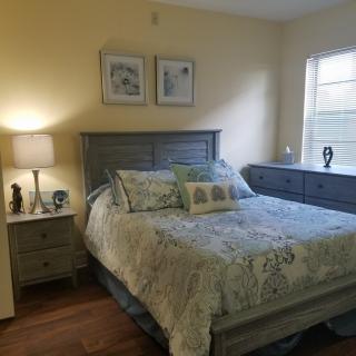 A cozy bedroom with a neatly made bed, bedside lamp, dresser, and window.