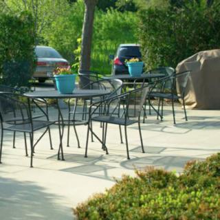 An outdoor patio with metal tables and chairs, featuring potted plants and parked cars in the background.