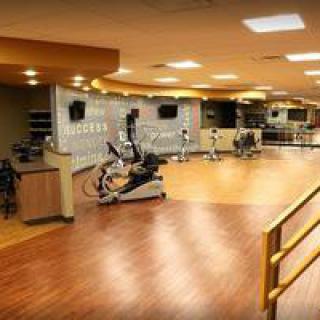A spacious gym with various exercise equipment and a wooden floor.