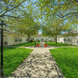 A tranquil courtyard with a central pathway, surrounded by lush greenery and buildings.