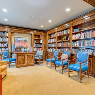 A cozy library room filled with books and wooden furniture, featuring artwork on the wall.