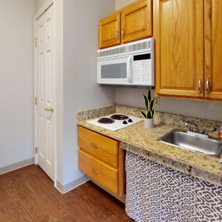 A compact kitchen with wooden cabinets, a granite countertop, a built-in microwave, and a small stovetop.