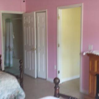 A cozy bedroom with pink walls featuring open doors and classic wooden furniture.