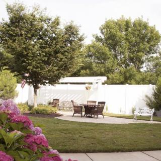 A serene backyard garden with outdoor furniture set on a patio, surrounded by lush trees and blooming flowers.