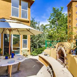 A sunny outdoor patio with a table, umbrella, and a brick oven surrounded by plants.