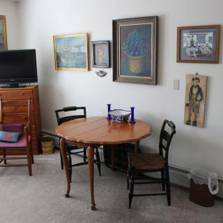 A cozy living room with a round dining table, surrounded by chairs and decorated with various artworks on the walls.